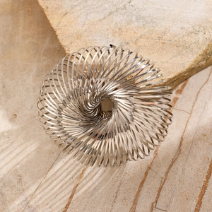 Macro shot of polished silver spiral metal bracelet on textured natural stone background