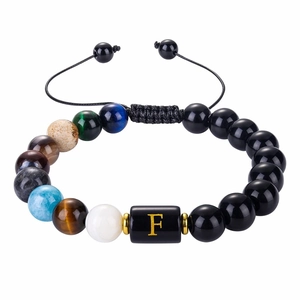 Close-up of black onyx bead bracelet with a gold letter F charm and galaxy-themed stones
