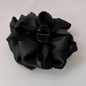 Detailed close-up of a black satin fabric flower hair claw clip on grey background