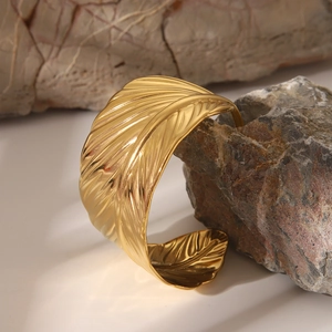 Dettaglio macro della piuma dorata su un bracciale rigido aperto in acciaio inossidabile