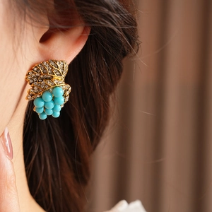 Macro shot of vintage gold grape earrings with teal beads and sparkling crystals on ear