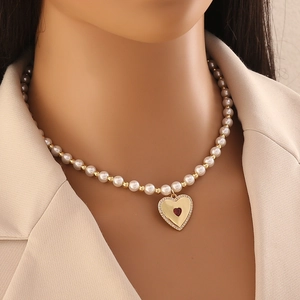 Faux pearl beaded necklace with gold heart pendant and red gemstone on a model neck