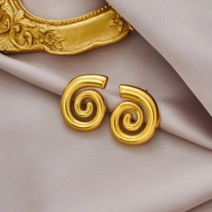 Vue détaillée de boucles d'oreilles spirales dorées polies sur un tissu en soie violette