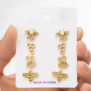 Set of four gold stainless steel bee and honeycomb stud earrings on a display card