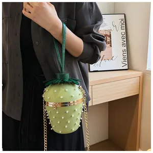 Détails d'un sac vert en forme de fraise avec rivets perlés blancs et chaîne dorée