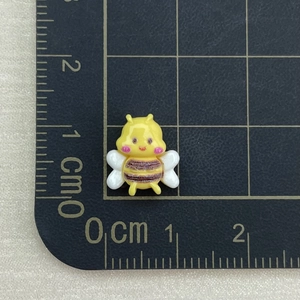 Close-up of a 1.5cm yellow resin bee charm on a grid ruler for nail art and DIY decor