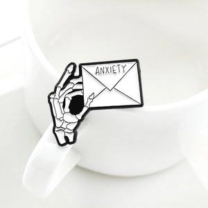 Punk style skull hand holding an anxiety letter enamel pin on a white ceramic mug