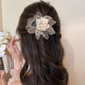 Detail of a beige mesh rose hair claw with pearl center worn on long wavy hair