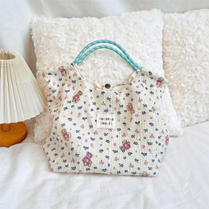 Detail of quilted bear floral canvas tote with blue rope handles on a cozy bed setup
