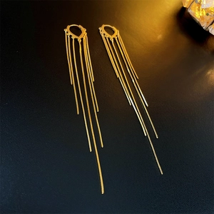 Macro detail of gold-plated heart tassel earrings on black textured backdrop