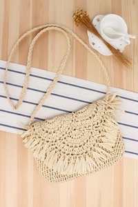 Detail of beige hand-woven crochet bag with long fringe tassels on a wooden surface