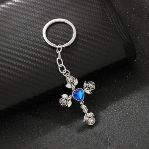 Detailed close-up of gothic silver cross keychain with blue heart gem on black surface