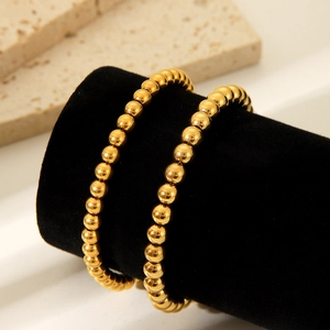 Minimalist 18K gold stainless steel bead bracelet for women displayed on a black stand