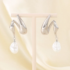 Detail of silver twisted metal earrings with hanging baroque pearls on beige silk fabric
