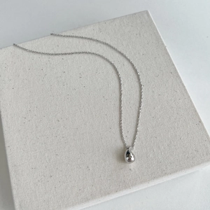 Minimalist silver chain necklace featuring a sleek teardrop pendant on a textured white block