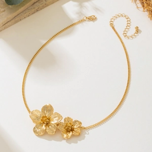 Détail d'un collier doré avec pendentif double fleur et chaîne fine avec fermoir mousqueton