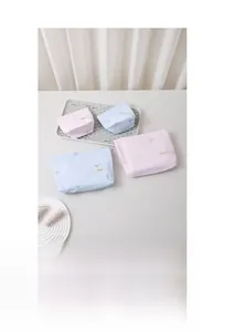 Détail de trousses de maquillage roses et bleues avec broderie nœud et étiquette HER BAG