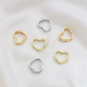 Detailed view of gold and silver heart pendants with zircon stones on white silk fabric