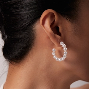 Close-up of large white pearls on C-shaped titanium steel hoop earrings worn by a model