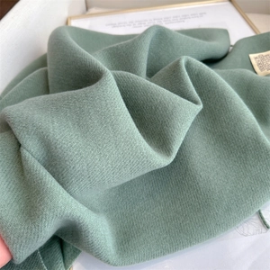 Detailed close-up showing soft texture and fabric label of green cashmere-like winter scarf
