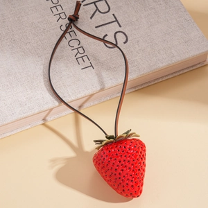Close-up of a realistic red resin strawberry pendant with a brown leather cord necklace