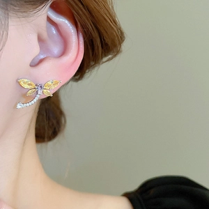 Macro detail of dragonfly stud earring with yellow and purple stones worn on the ear