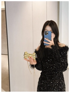 Detailed view of model holding a gold bow-shaped metal clutch with sequin dress