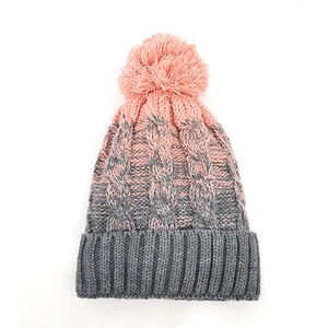 Dettaglio di un berretto in maglia a trecce rosa e grigio con pompon soffice