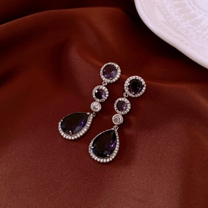 Detail of silver drop earrings with purple crystals on elegant burgundy satin fabric