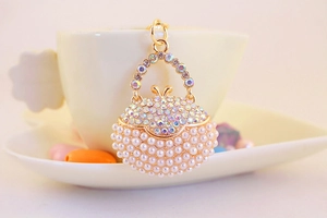 Detail of a golden handbag keychain with white pearls and iridescent rhinestones