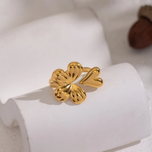 Macro shot of gold floral heart ring with four-leaf clover design on white stone stand