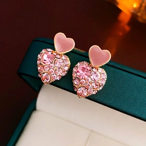 Pink heart-shaped stud earrings with sparkling crystals on green jewelry box display