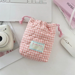 Pink and white checkered quilted drawstring camera bag shown on a desk with a polaroid