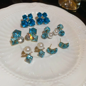 Close-up of square green crystals and white pearls set in 18k gold plated stud earrings