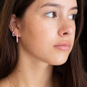 Close-up of a model wearing C-shaped pink and purple enameled earrings in gold finish