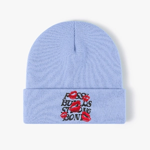 Detail of light blue knit beanie with black embroidered text and red lip prints