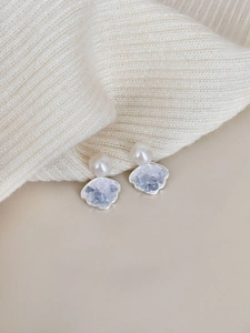 Macro detail of silver shell earrings with pearls and blue crystals on knit fabric