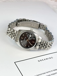 Macro detail of silver stainless steel watch strap and dark brown sunray dial with date