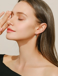 Detail of silver hoop earring with rectangular green stone on a female model