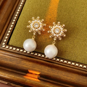 Détail de boucles d'oreilles flocon dorées avec perles blanches sur velours vert olive