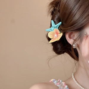 Detail of teal starfish and yellow flower hair clip worn on a brown braided updo