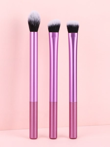 Détail de trois pinceaux à maquillage violets avec poils dégradés sur un fond rose doux