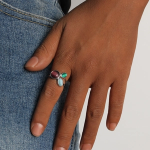 Gros plan d'une bague en argent avec des pierres précieuses rouges, vertes et bleues au doigt