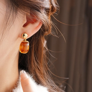 Close-up of 18K gold plated resin earring with amber oval stone on female model