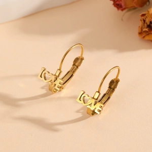 Detailed view of gold LOVE earrings with French hooks on a romantic beige background