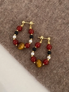Close-up of tiger eye and pearl beaded hoop earrings on a warm knit texture