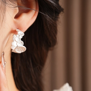 Gros plan de boucles d'oreilles créoles argentées texturées portées par un mannequin