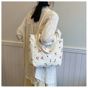 Detail of corduroy tote bag featuring red cherry prints and front pocket on shoulder strap