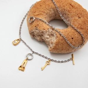 Détail des pendentifs serrure et clé dorés sur un collier à boucle OT et un donut