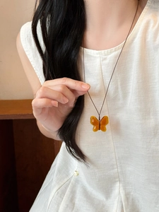 Detail of amber resin butterfly pendant necklace on model with minimalist brown cord